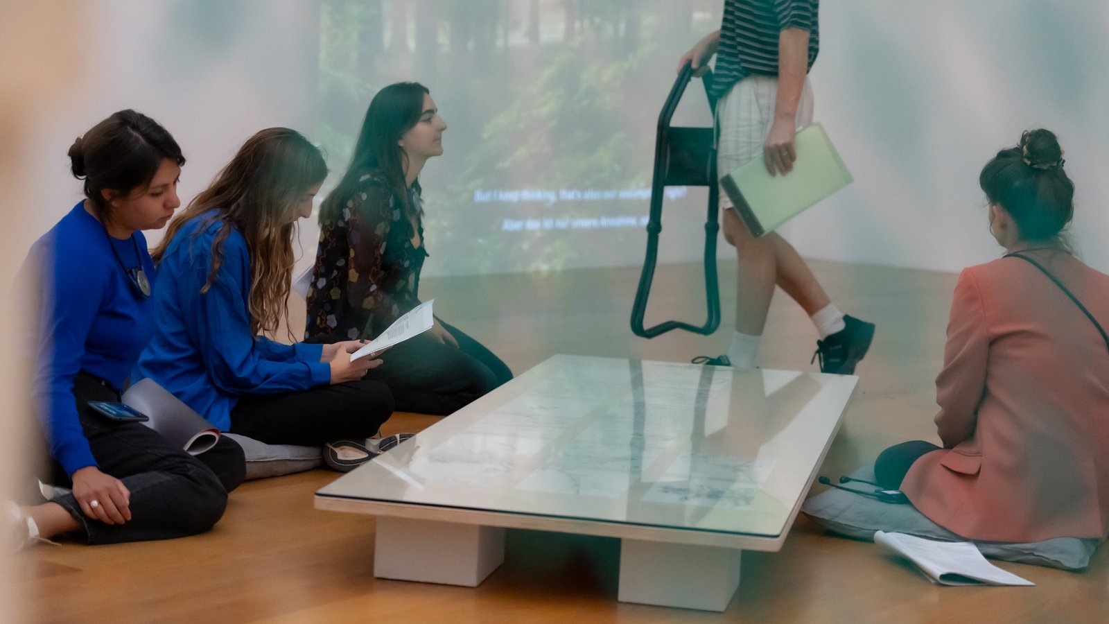 Teilnehmende sitzen während des Kumu Symposiums „Agency of Plants“ vor einer Projektion in einem Ausstellungsraum.