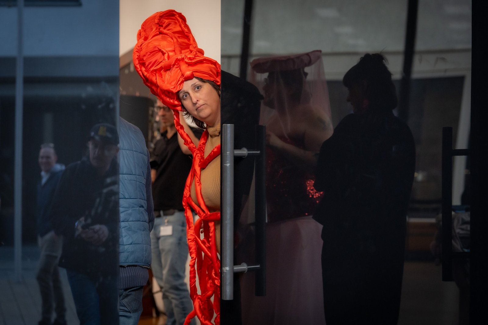 Person mit auffälligem orangefarbenem Kostüm steht während einer Vernissage hinter einer Glastür.