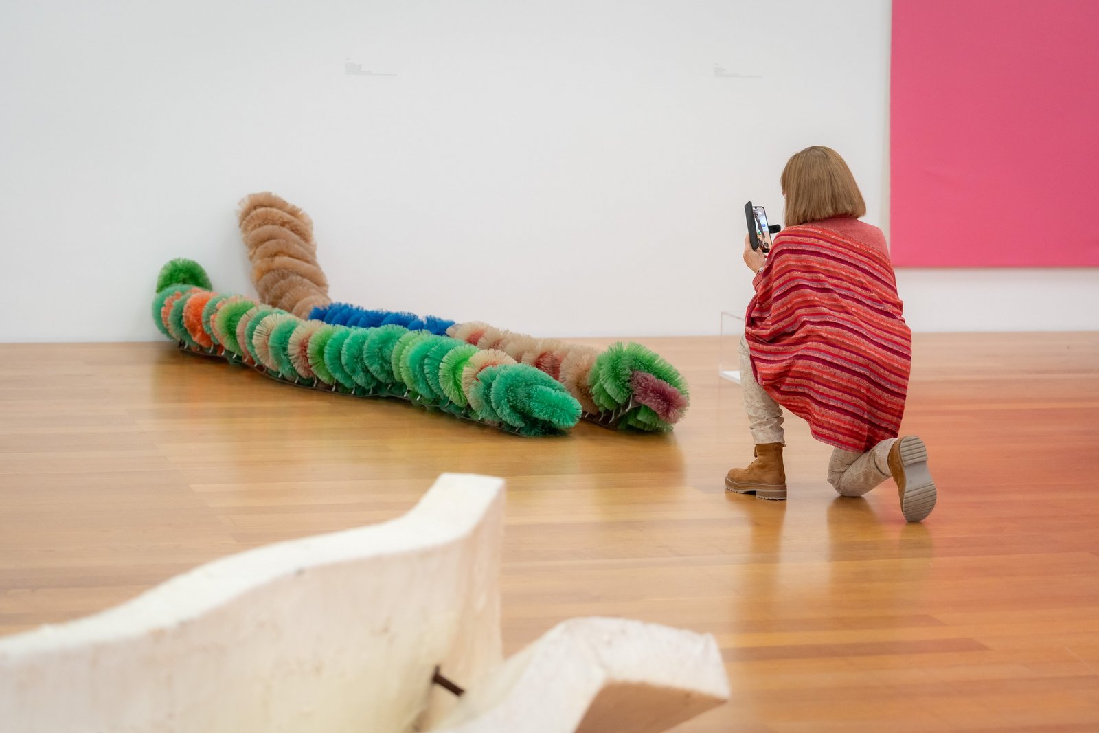 Eine Frau kniet im Museum und fotografiert ein buntes Kunstwerk auf dem Boden.