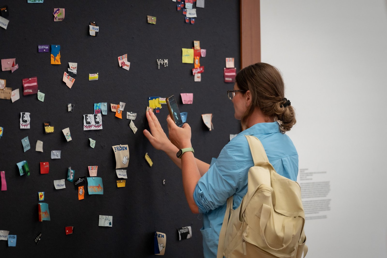 Besucherin fotografiert kleine Ausstellungsstücke an einer schwarzen Wand.