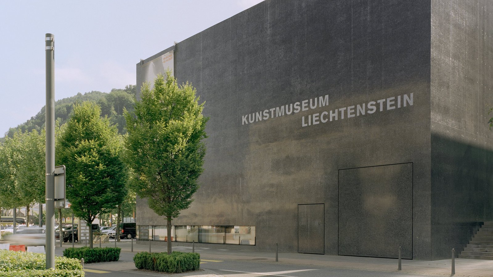 Außenansicht des Kunstmuseum Liechtenstein mit dunkler Fassade, Bäumen und Straße im Vordergrund.