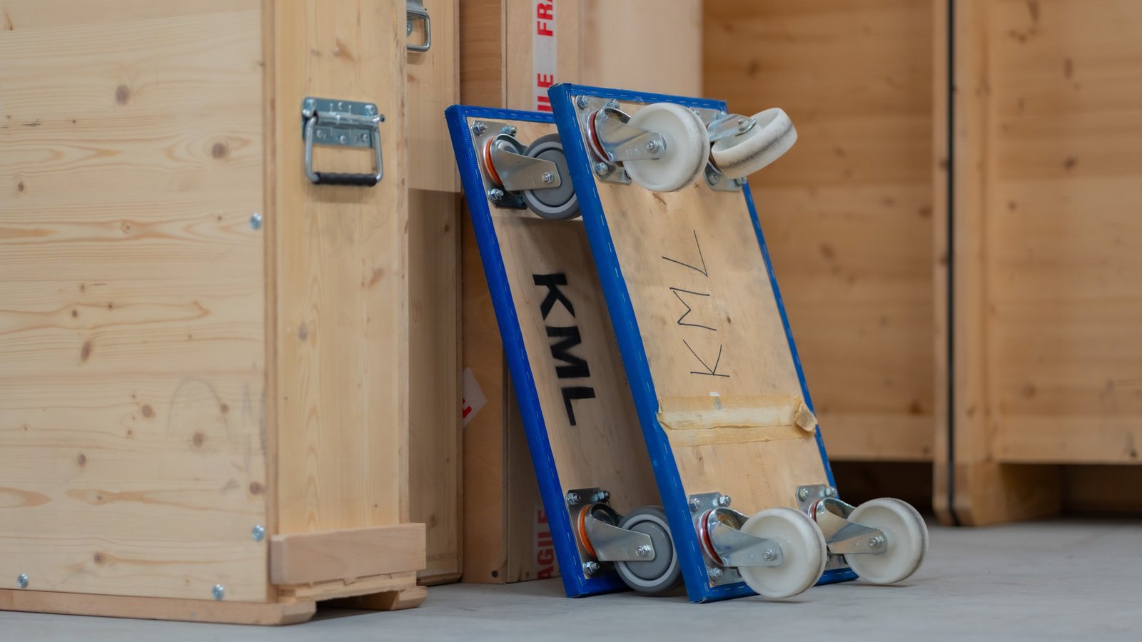 Zwei KML-Möbelroller lehnen an Holzkisten.